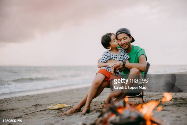 young girl kissing her father on beach with campfire - アウトドア　日本人 ストックフォトと画像