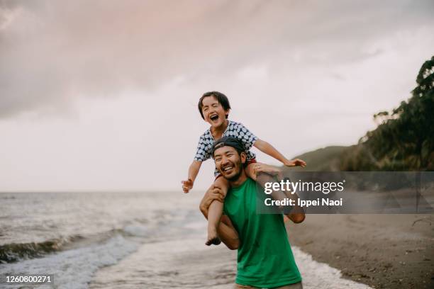 happy father carrying child on shoulders and running on beach - bära på axlarna bildbanksfoton och bilder