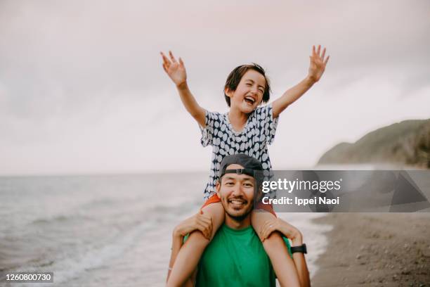 father carrying cheerful daughter on shoulders on beach - dad cheering stock pictures, royalty-free photos & images