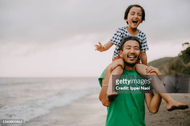 cheerful father carrying his daughter on shoulders on beach - kindertijd stockfoto's en -beelden
