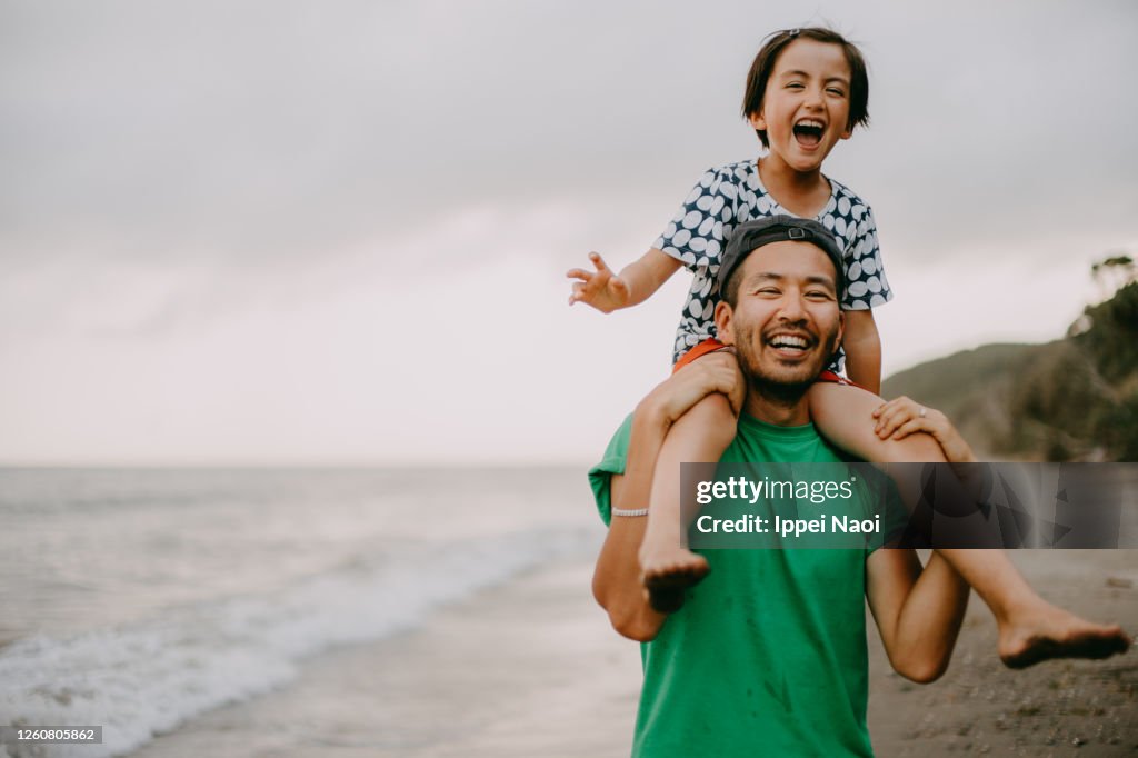 Cheerful father carrying his daughter on shoulders on beach
