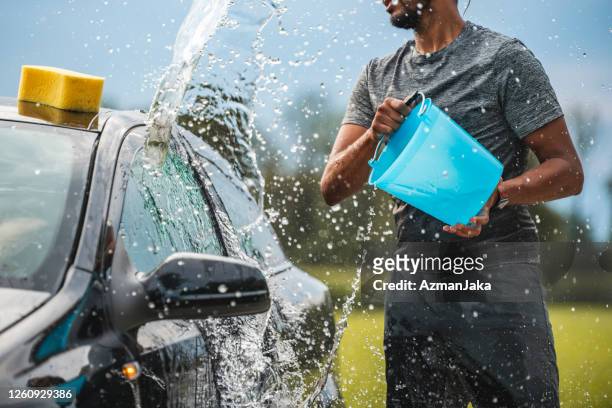 mixed race young adult reinigung des autos mit wasser - bucket stock-fotos und bilder