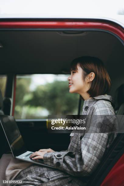 junge asiatische geschäftsfrau sitzt auf dem rücksitz eines taxis, das auf laptop arbeitet, während sie in der stadt pendelt - mobility as a service stock-fotos und bilder