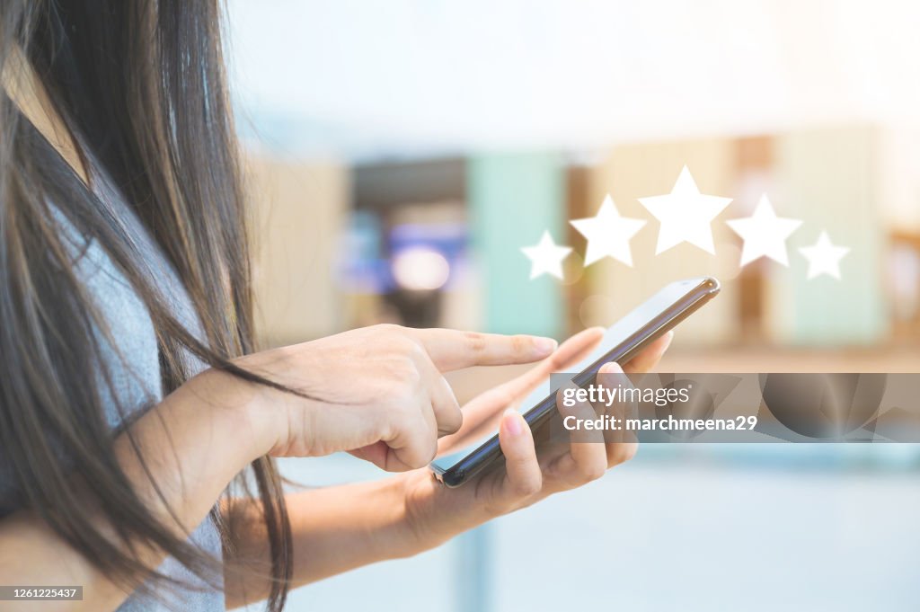 Customer service experience and business satisfaction survey. Close-up image of woman hand using mobile smart phone with icon five star symbol to increase rating of company concept