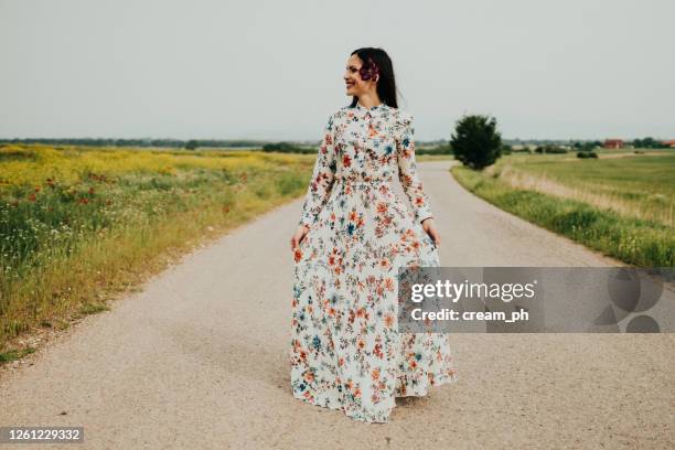 frau trägt ein kleid zu fuß an einem sonnigen tag in der natur - floral pattern dress stock-fotos und bilder