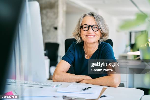 smiling businesswoman at desk in office - mature adult stock pictures, royalty-free photos & images