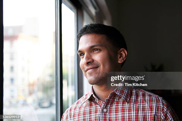 smiling man in plaid shirt near window - man looking through window stock pictures, royalty-free photos & images