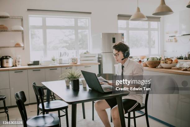 an asian chinese young adult man with tie, long sleeve shirt and short pant sitting using laptop in his dining room for video conference with his business partner and colleague virtual business meeting - conference dining table stock pictures, royalty-free photos & images