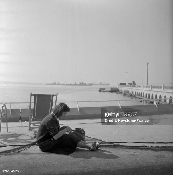 Une femme, assise par terre, répare un filet de pêche sur port de Cannes, France en avril 1957.