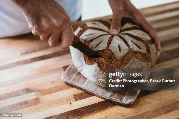 a man slicing a wholemeal sourdough bread - bread knife stock-fotos und bilder