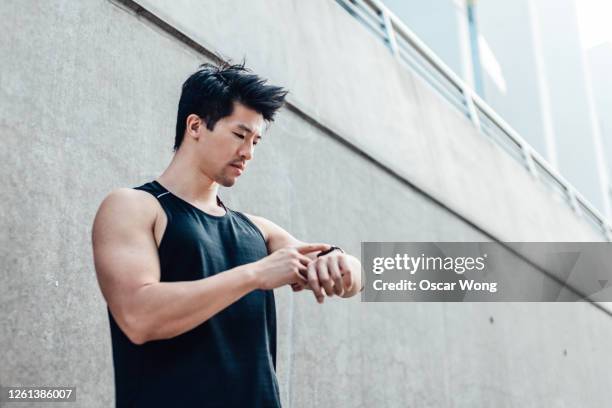 motivated young man using running app on smart watch in the city - runner man stock pictures, royalty-free photos & images