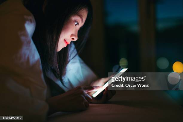 young woman using smart phone underneath duvet in the dark - scrolling - fotografias e filmes do acervo