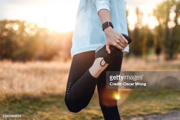 young woman stretching legs in the park after exercise - esercizio fisico foto e immagini stock