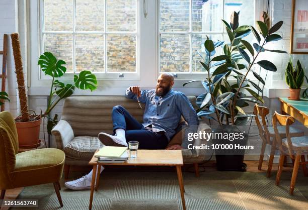 confident businessman taking break in office - office sofa stock-fotos und bilder