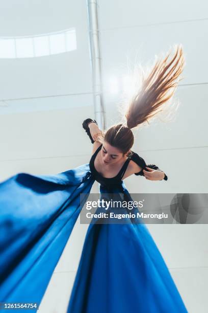 female acrobat aerialist practicing, suspended from a length of blue silk. - luftakrobat stock-fotos und bilder