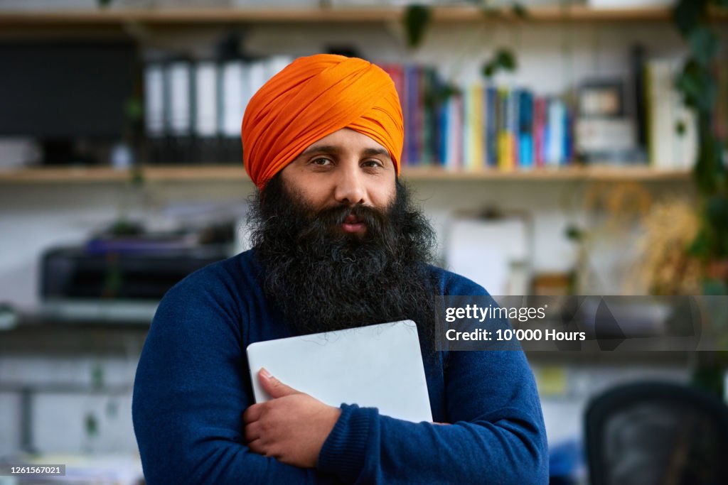 Sikh man holding laptop, looking at camera