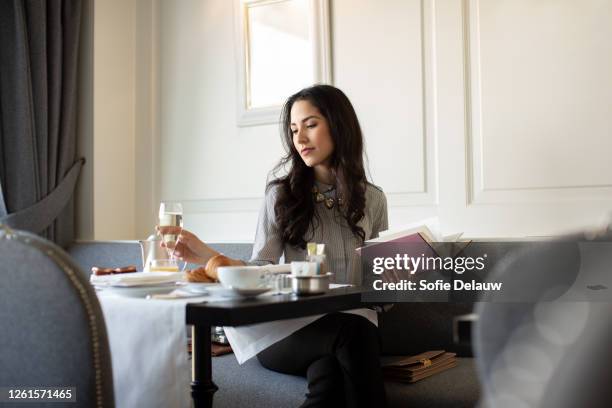 woman with long black hair wearing glasses sitting at a restaurant table, holding book. - 昼休み ストックフォトと画像