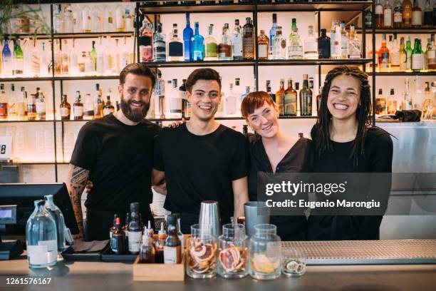portrait of two young women and men wearing black clothes, working in bar, smiling at camera. - bartender foto e immagini stock
