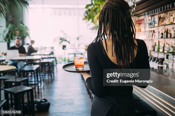 rear view of waitress wearing black clothes working in bar, carrying drinks on a tray. - empregada de mesa imagens e fotografias de stock