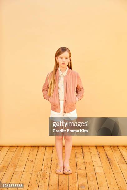 portrait of girl with long blond hair wearing shorts, shirt and pink jacket, on pale yellow background. - 13 year old girls in shorts stock pictures, royalty-free photos & images