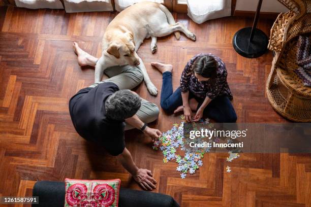 father and daughter sitting on living room floor, doing jigsaw puzzle during coronavirus lockdown. - rompicapo foto e immagini stock
