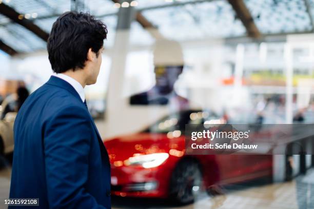 businessman looking through glass wall at sports car in showroom - sports car showroom stock pictures, royalty-free photos & images