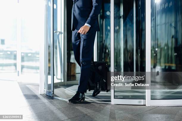 businessman with wheeled luggage exiting revolving doors of building - revolving door ストックフォトと画像