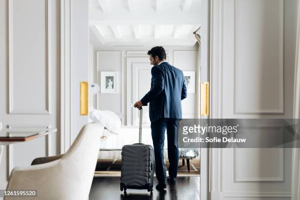 businessman with wheeled luggage in suite - vista posteriore foto e immagini stock
