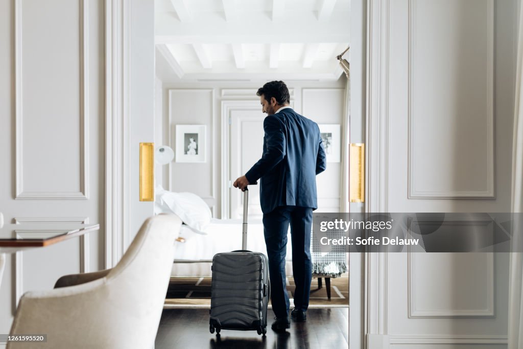 Businessman with wheeled luggage in suite