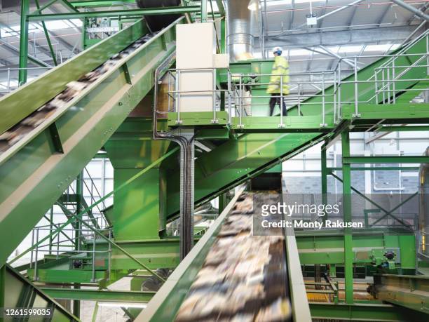 worker checking conveyor belts with waste paper in waste recycling plant. - centro di riciclaggio foto e immagini stock