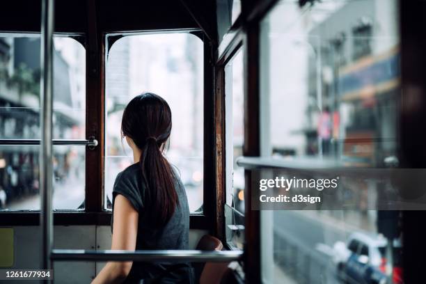 young asian female traveller exploring the city, looking through window while riding local city tram enjoying the city scene - straßenbahnstrecke stock-fotos und bilder