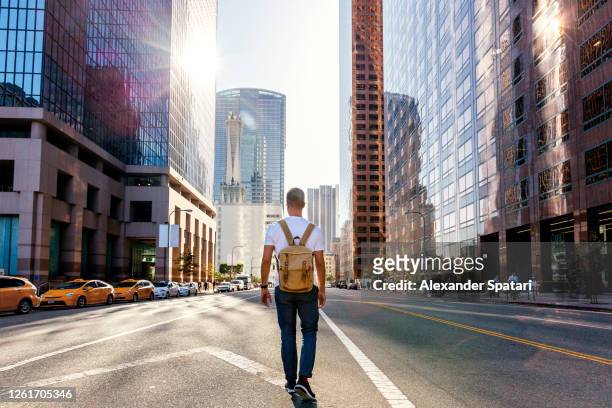 young man with backpack walking on the street in los angeles downtown, california, usa - los angeles città foto e immagini stock