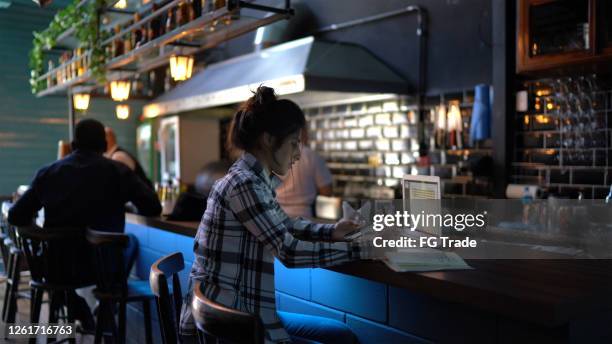 young woman working or studying in a bar, using laptop and smartphone - busy bar stock pictures, royalty-free photos & images