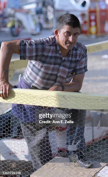 Portrait of a carnival worker as he stands, one leg up on a box, as he stands behind chicken wire at the Sangamon County Fair, New Berlin, Illinois,...