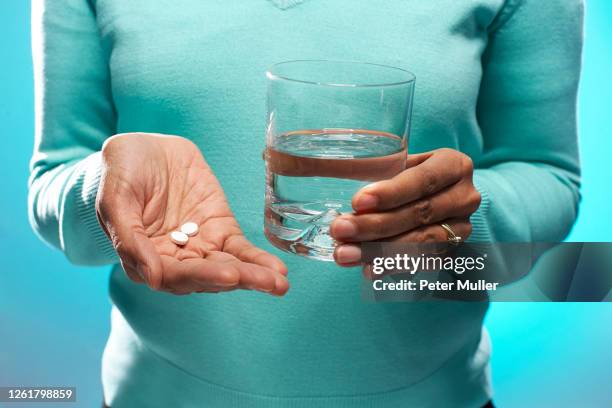 close up of woman holding tablets and glass of water, on blue background. - taking medication stockfoto's en -beelden