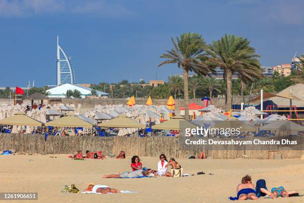 dubai, united arab emirates - tourists and local residents seen sunbathing in the afternoon sun on umm suqeim beach; in the far background, a few kilometers away, is the burj al arab hotel. copy space. - dubai jbr stock pictures, royalty-free photos & images