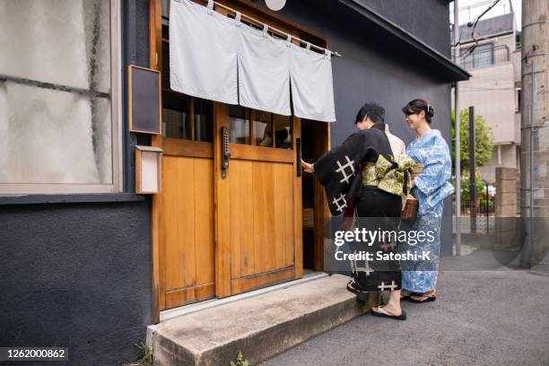 japanese female friends in yukata entering traditional japanese ‘ryokan’ hotel - noren stock pictures, royalty-free photos & images