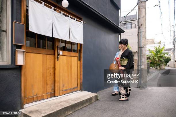 japanese female friends in yukata entering traditional japanese ‘ryokan’ hotel - noren stock pictures, royalty-free photos & images