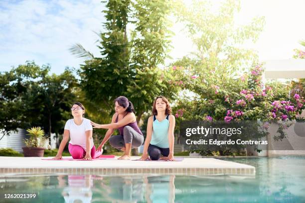 una mujer enseñándole yoga a dos niñas frente a una piscina - mujer yoga stock pictures, royalty-free photos & images