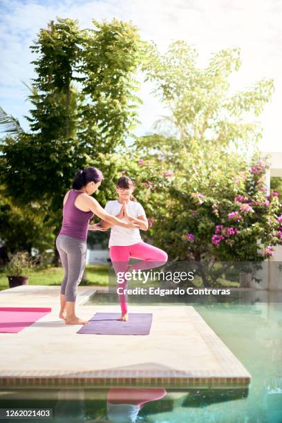 una mujer enseñándole yoga a una niña frente a una piscina - niña isolated stock-fotos und bilder