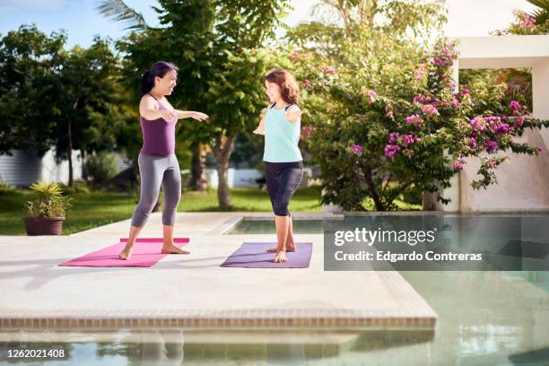 una mujer enseñándole yoga a una niña frente a una piscina - niña isolated stock-fotos und bilder