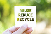 Holding the paper with REUSE REDUCE RECYCLE message in front of a beautiful blur nature background