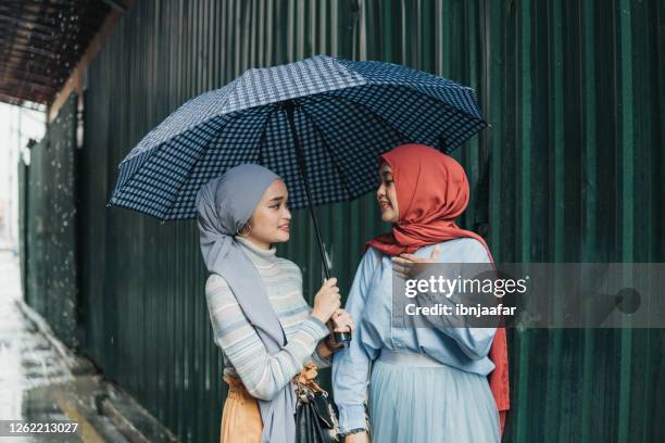 asian women sharing umbrella with friends at town - sharing umbrella stock pictures, royalty-free photos & images