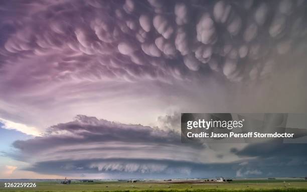 a massive tornado super-cell with mammatus, arcus, tail cloud, and wall cloud, illuminated at sunset with pink and blue colours - mammatus cloud stock pictures, royalty-free photos & images