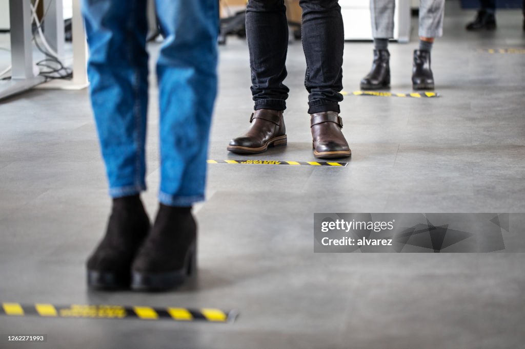 Uomini d'affari in piedi dietro la segnaletica di distanziamento sociale sul pavimento dell'ufficio