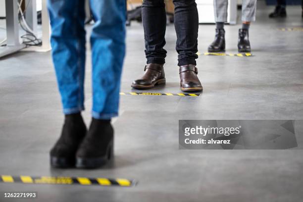 business people standing behind social distancing signage on office floor - covid 19 stock pictures, royalty-free photos & images