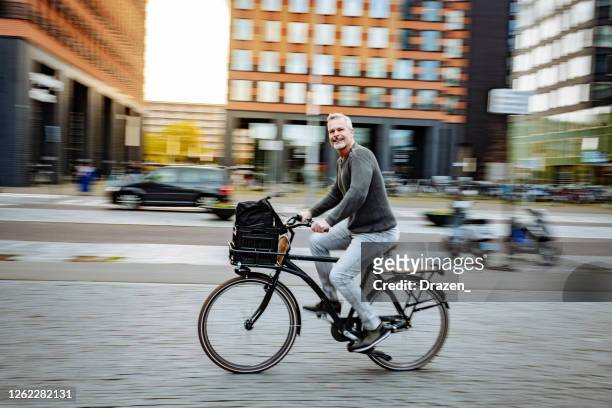 mature essential worker in city, riding bicycle while going to work - netherlands stock pictures, royalty-free photos & images