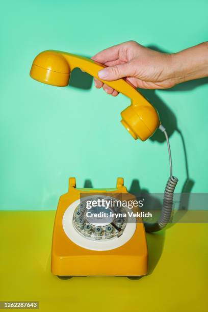 hand of a senior woman and yellow handset of a retro telephone on mint green background. - telephone receiver stock pictures, royalty-free photos & images
