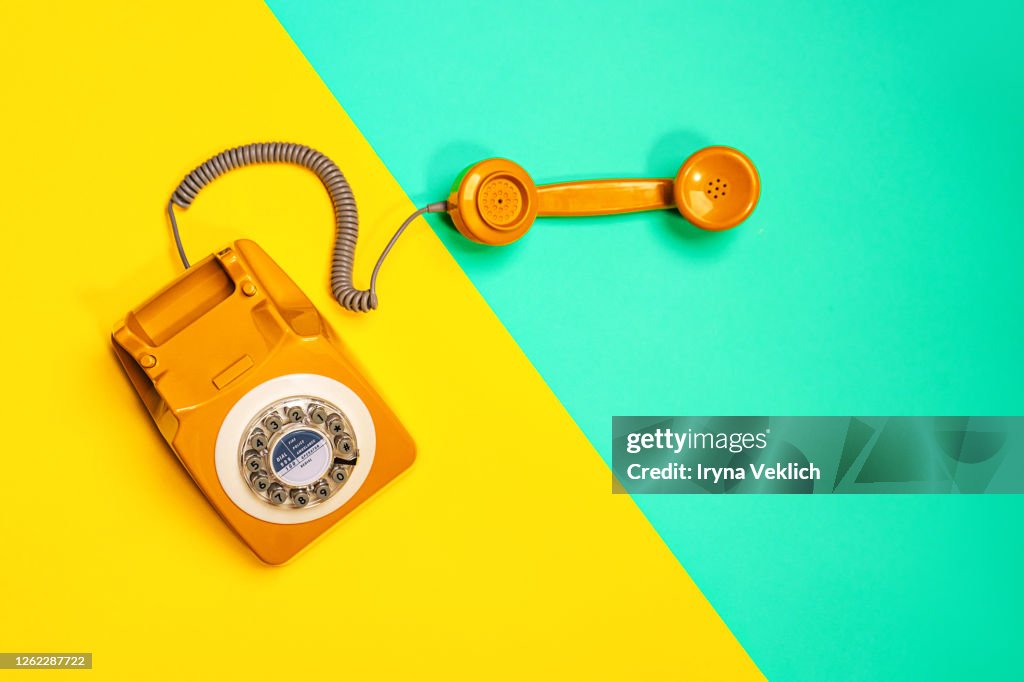 Yellow handset of a retro telephone on yellow and mint green background.