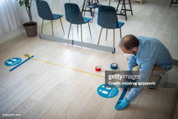 man with protective gloves putting adhesive tape on six feet distance in front of bank counter - two meters stock pictures, royalty-free photos & images